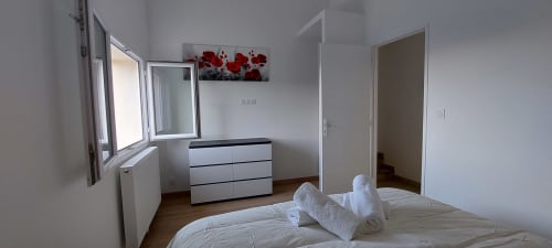 Chambre lumineuse au gîte Le Mas de Trépeloup à Alès avec lit blanc, commode, fenêtre, tableau floral rouge et salle de bain privée