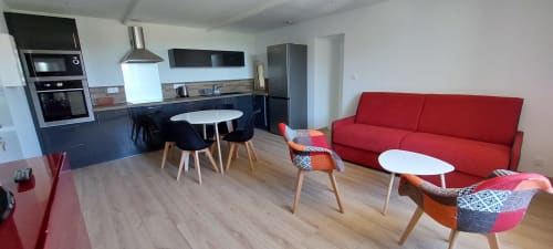 Espace de vie ouvert et moderne au gîte Le Mas de Trépeloup à Alès avec canapé rouge, cuisine et table à manger