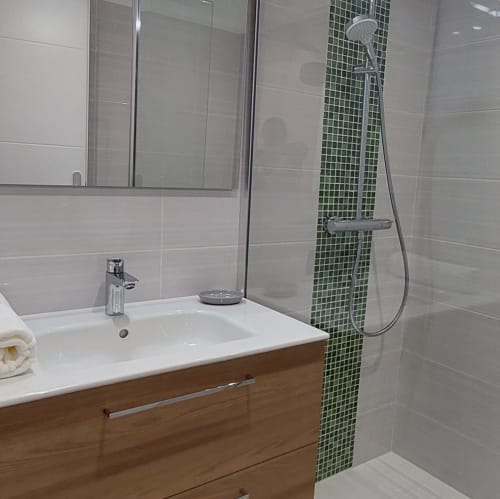 Salle de bain moderne du Mas de Trépeloup avec lavabo blanc, meuble en bois, pomme de douche pluie et carrelage mosaïque vert