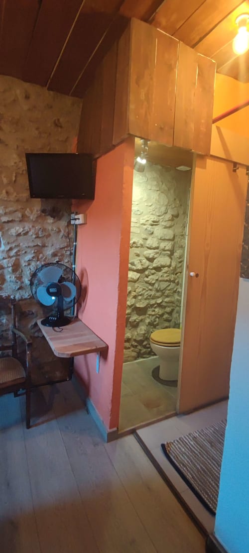 Habitación del hostel La Calma De Bellver con TV, escritorio, ventilador y baño privado con paredes de piedra