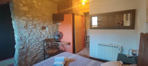 Acogedora habitación en el hostal La Calma De Bellver con paredes de piedra, cama, escritorio, ventilador, radiador y espejo