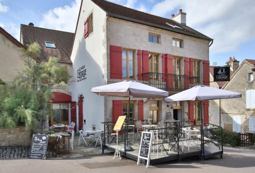La Maison George hotel with red shutters, outdoor terrace seating, umbrellas, and stone architecture in Flavigny-sur-Ozerain,