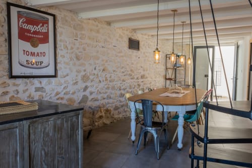 Salle à manger du Mas Lafleur à Châteaurenard avec murs en pierre apparente, luminaires suspendus modernes et table en bois