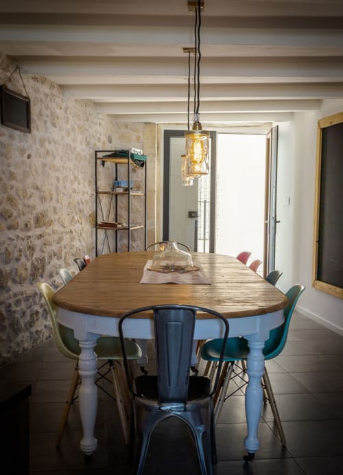 Salle à manger Mas Lafleur avec table en bois, chaises colorées, suspension et mur en pierre à Châteaurenard