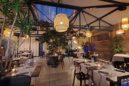 Elegant dining area at Les Gites de Campardon with woven pendant lights, plants, and twilight views in Monties