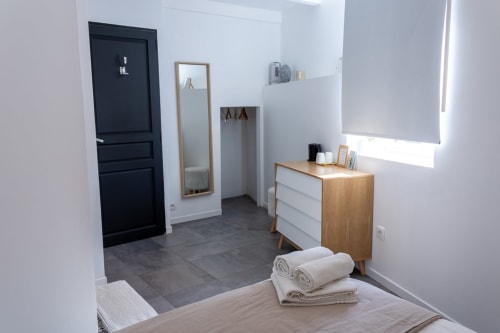 Gandhi-Zimmer im Mas Lafleur Châteaurenard: modernes Schlafzimmer mit Holzmöbeln, Spiegel, dunkler Tür, aufgerollten Handtüchern und natürlichem Licht