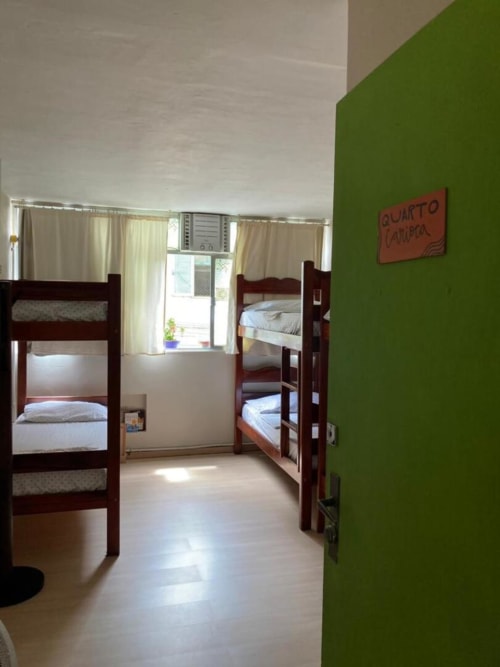 Quarto de dormitório iluminado no Hostel New Ipanema com beliches de madeira, parede verde e grandes janelas