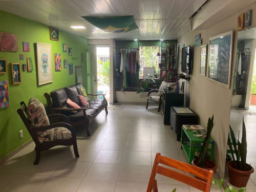 Área comum clara no Hostel New Ipanema com paredes verde-limão, móveis pretos, arte e araras de roupas no Rio de