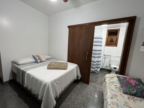 Quarto aconchegante no Pouso do Barão com cama, acesso ao banheiro e vista para o jardim em Domingos Martins