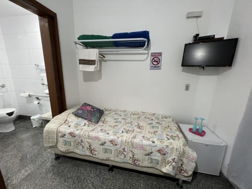 Quarto simples do Pouso do Barão com cama, TV, banheiro e placa de proibido fumar