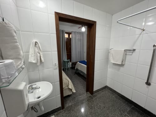 Banheiro moderno do Hotel Pouso do Barão em Domingos Martins com azulejos brancos, pia, chuveiro e vista para o quarto