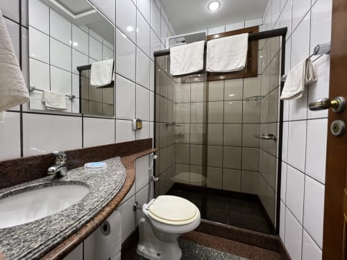 Banheiro moderno no hotel Pouso do Barão em Domingos Martins com bancada de granito, chuveiro amplo e azulejos brancos.