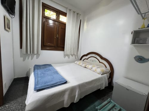 Quarto aconchegante no Pouso do Barão com cama de madeira, manta azul, lençóis brancos e vista para o jardim em Domingos Martins