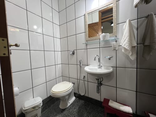 Banheiro moderno do hotel Pouso do Barão em Domingos Martins com azulejos brancos, vaso sanitário, pia e espelho.