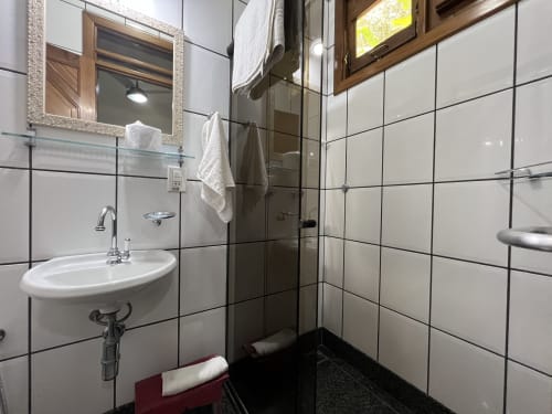 Banheiro moderno no Pouso do Barão com azulejos brancos, chuveiro tipo chuva e janela com vista para o jardim