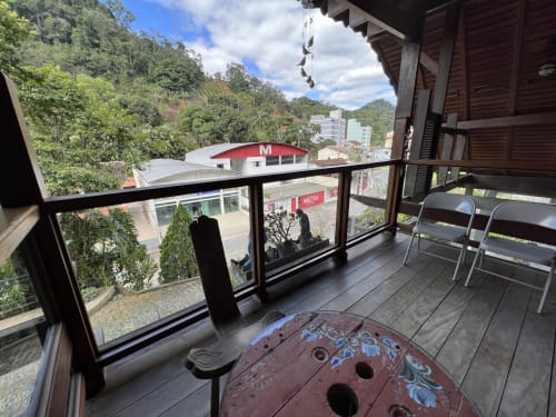 Varanda do Hotel Pouso do Barão em Domingos Martins com vistas de montanha, deck de madeira, cadeiras e floresta ao fundo
