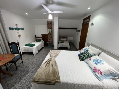 Quarto espaçoso no hotel Pouso do Barão em Domingos Martins com várias camas, ventilador de teto e acabamentos em tijolos rústicos