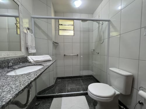 Banheiro moderno no hotel Pouso do Barão em Domingos Martins com bancada em granito, boxe de vidro e azulejo branco