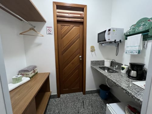 Kitchenette do quarto do hotel Pouso do Barão com porta de madeira, bancada de granito, micro-ondas e cafeteira em Domingos Martins