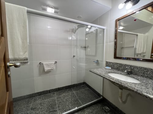 Banheiro moderno com chuveiro de vidro, bancada em granito e pias duplas no hotel Pouso do Barão em Domingos Martins