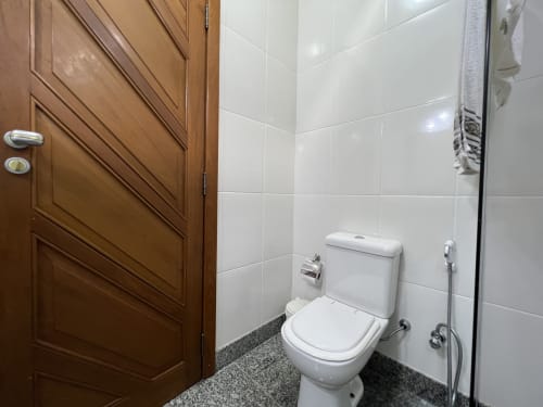 Banheiro moderno no hotel Pouso do Barão em Domingos Martins com paredes de azulejos brancos, sanitário, chuveiro e porta de entrada em madeira