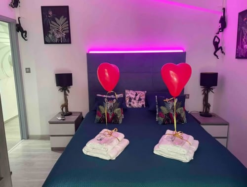 Chambre romantique au Gîte du Miroir avec néons en forme de cœur, éclairage rose ambiant et équipements spa