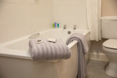 Gray towels draped over bathtub edge in Sliabh Beagh Hotel bathroom with toilet visible