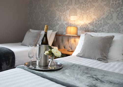 Elegant hotel room at Sliabh Beagh with champagne, glasses, and flowers on bed, damask wallpaper backdrop