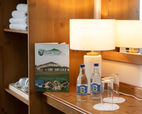 Sliabh Beagh Hotel room amenities: white towels, lamp, water bottles, and welcome brochure on wooden desk