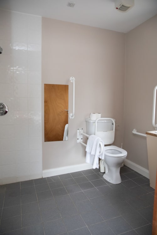 Accessible bathroom at Sliabh Beagh Hotel with white tile shower, toilet, grab bars, and dark tile flooring
