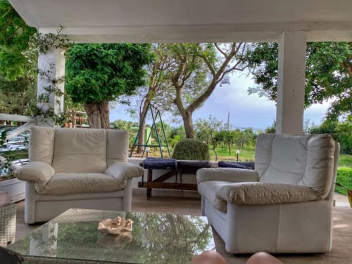 Terrazza coperta spaziosa presso Agriturismo Il Pomo d'oro con poltrone color crema, travi in legno e vista sui rigogliosi giardini