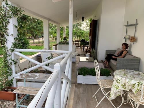Patio dell'Agriturismo Il Pomo d'oro con donna al riposo, ringhiere bianche, piante in vaso e vista sulla campagna di Assemini