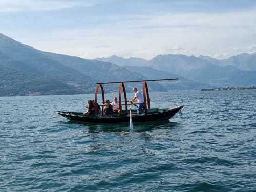 Traditional boat with passengers on Lake Como near Bellano, with mountain backdrop and clear alpine waters