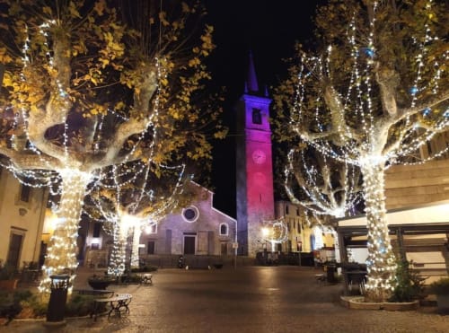 Illuminated Italian piazza at night with decorated trees and church tower, Bellano Como