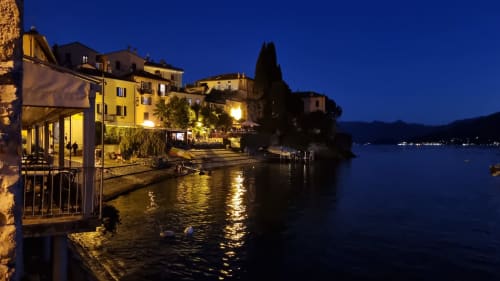 Waterfront villa at dusk in Bellano, Lake Como, with illuminated yellow buildings and dining terrace overlooking the calm