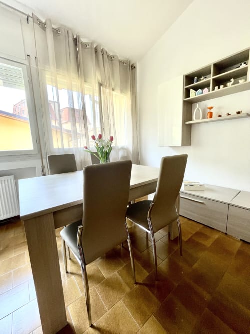 Elegante sala da pranzo dell'appartamento Varenna by Foot con tavolo bianco, sedie rivestite, scaffalature integrate e vista sulle montagne