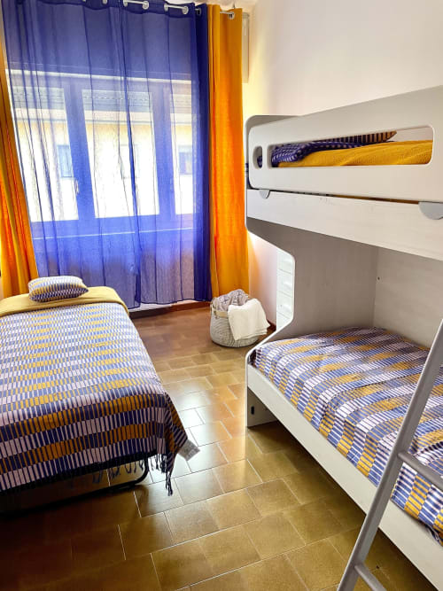 Luminosa camera nel dormitorio di Varenna by Foot con letto a castello, letto singolo, tende blu e vista sulle montagne di Varenna, Italia