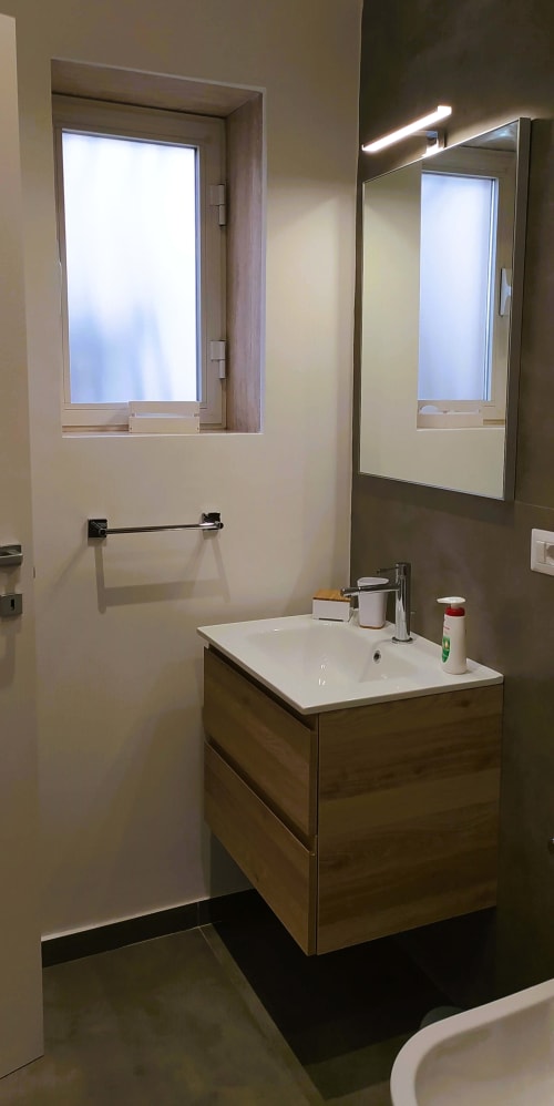 Bagno moderno a Bari con vanity in legno, specchio con illuminazione LED, finestra e lavabo bianco nell'appartamento