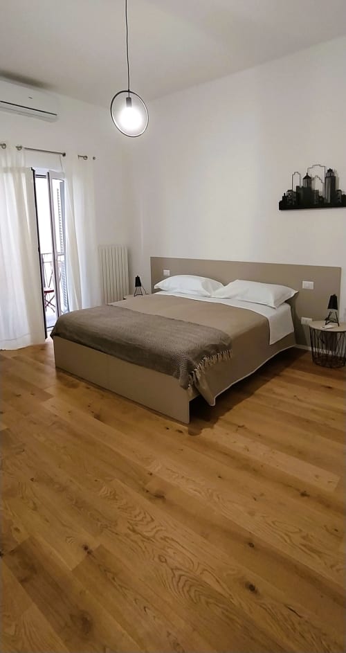 Camera da letto moderna a Bari Vacation con letto beige, lampada a sospensione, pavimenti in legno e vista sul giardino a Bari, Italia