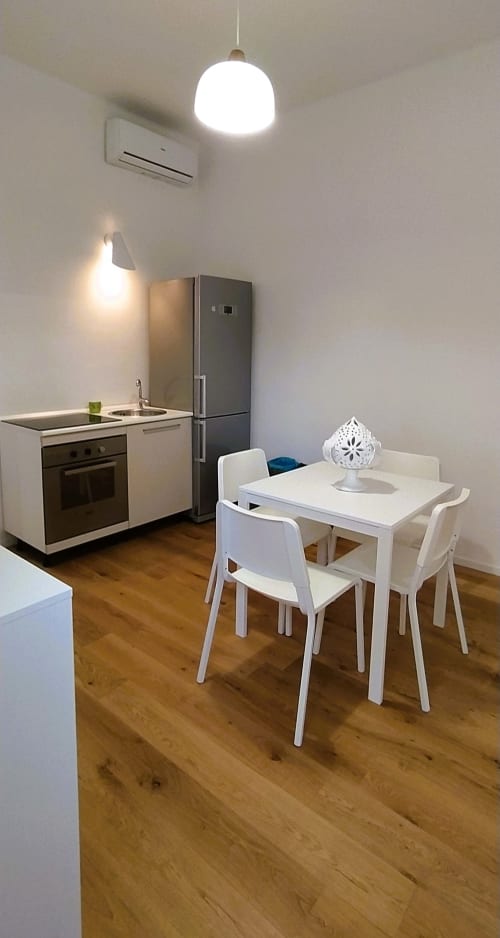 Cucina e zona pranzo moderna nell'appartamento di Bari con tavolo bianco, sedie, fornello, frigorifero e lampada a sospensione