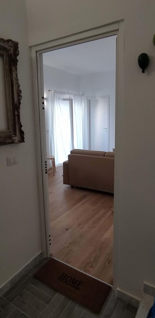 Varco aperto dall'ingresso al luminoso soggiorno con divano marrone dell'appartamento vacanze Bari, Via Genova 31