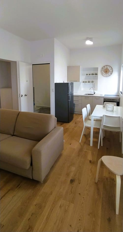 Moderno appartamento open-plan a Bari con divano beige, tavolo da pranzo, cucina e pavimenti in legno