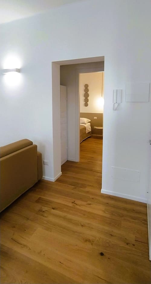 Ingresso moderno dell'appartamento Bari Vacation con pavimenti in legno, pareti bianche e porta aperta verso camera da letto con illuminazione calda