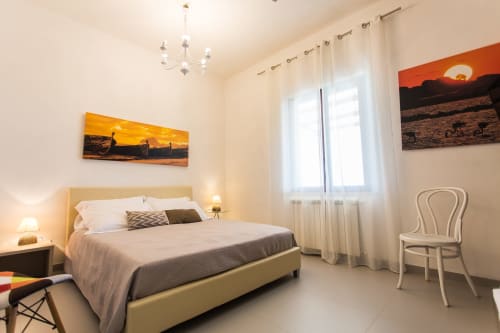 Modern bedroom at Villa Maria with sunset artwork, beige bed, white chair, and sea view at Sant'Andrea, Valderice