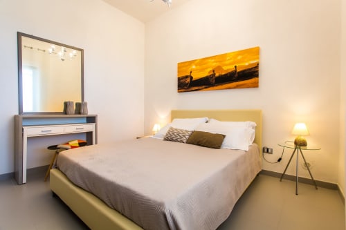 Modern bedroom at Villa Maria with yellow headboard, mirror vanity, and sunset boat artwork in Sant'Andrea, Valderice
