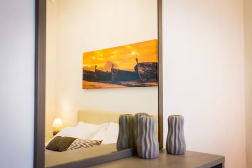 Bedroom mirror reflecting bed with yellow headboard, white pillows, and sunset boat artwork at Villa Maria una Finestra sul