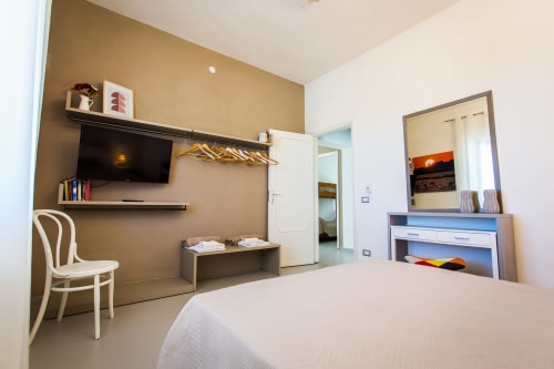 Modern bedroom at Villa Maria with tan accent wall, wall-mounted TV, wooden shelving, and sea view mirror
