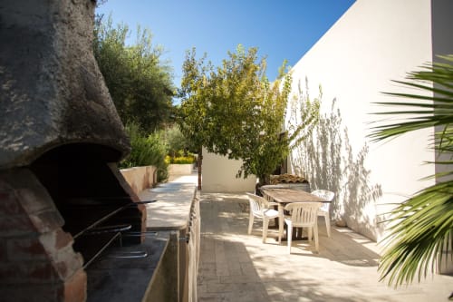 Sunny terrace at Villa Maria with white chairs, dining table, and Mediterranean plants overlooking Sant'Andrea, Valderice