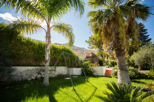 Lush garden with palm trees and swing at Villa Maria, Valderice Sicily overlooking Mediterranean