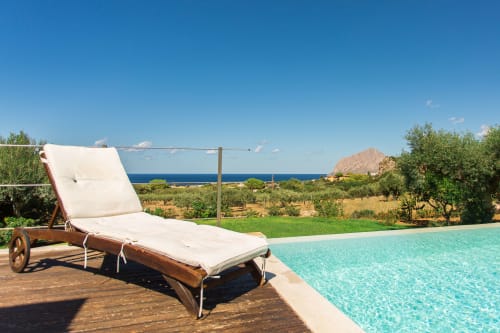 Wooden lounge chair with white cushions on deck beside turquoise pool overlooking Mediterranean Sea, Villa Maria, Valderice